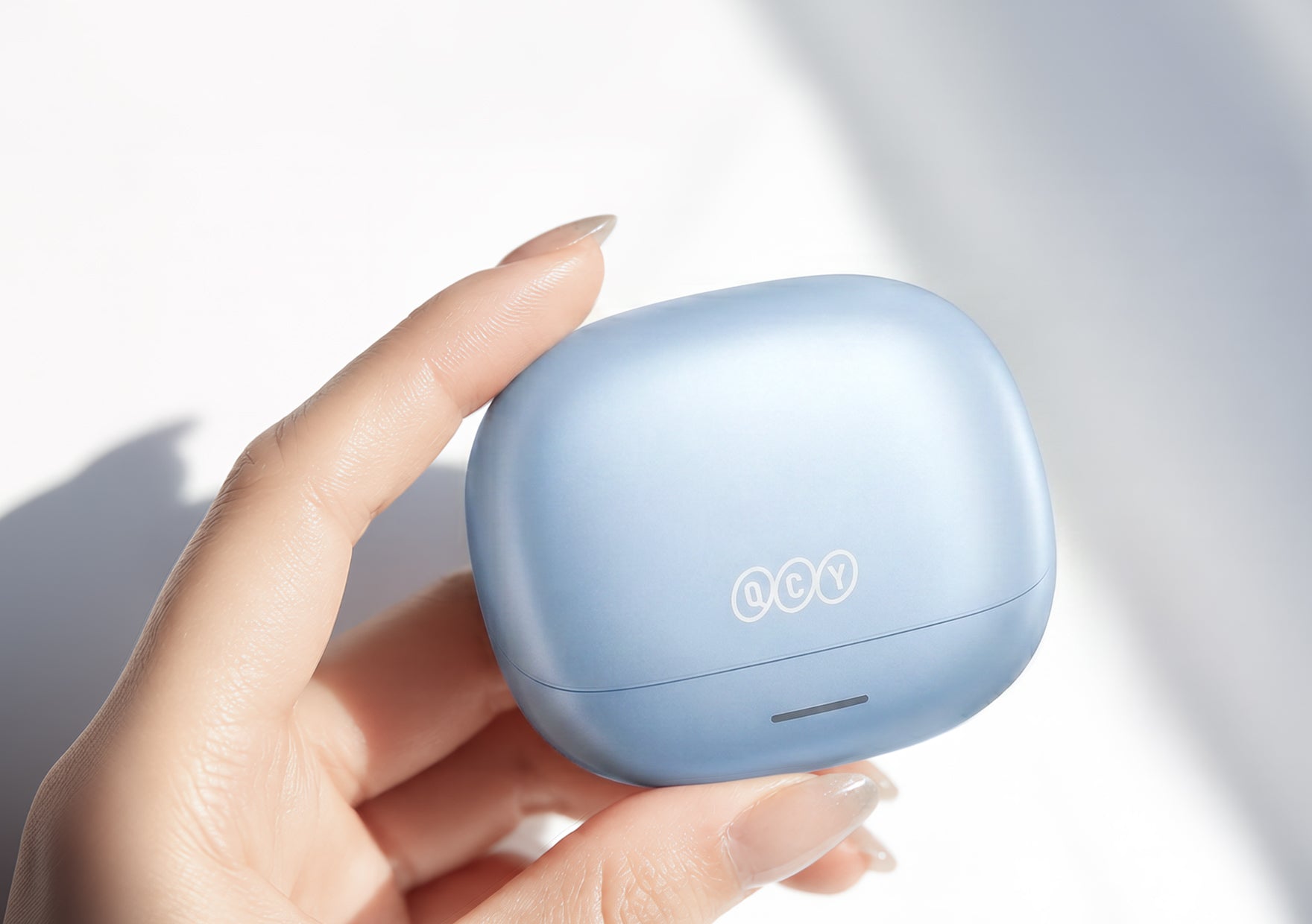 Cuffie Bluetooth QCY in azzurro chiaro, tenute nella custodia di ricarica.