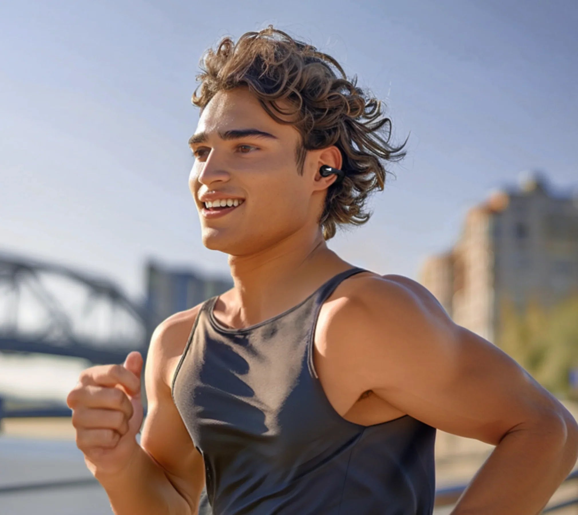 Giovane uomo sorridente che corre con auricolari wireless, abbigliamento sportivo all'aperto