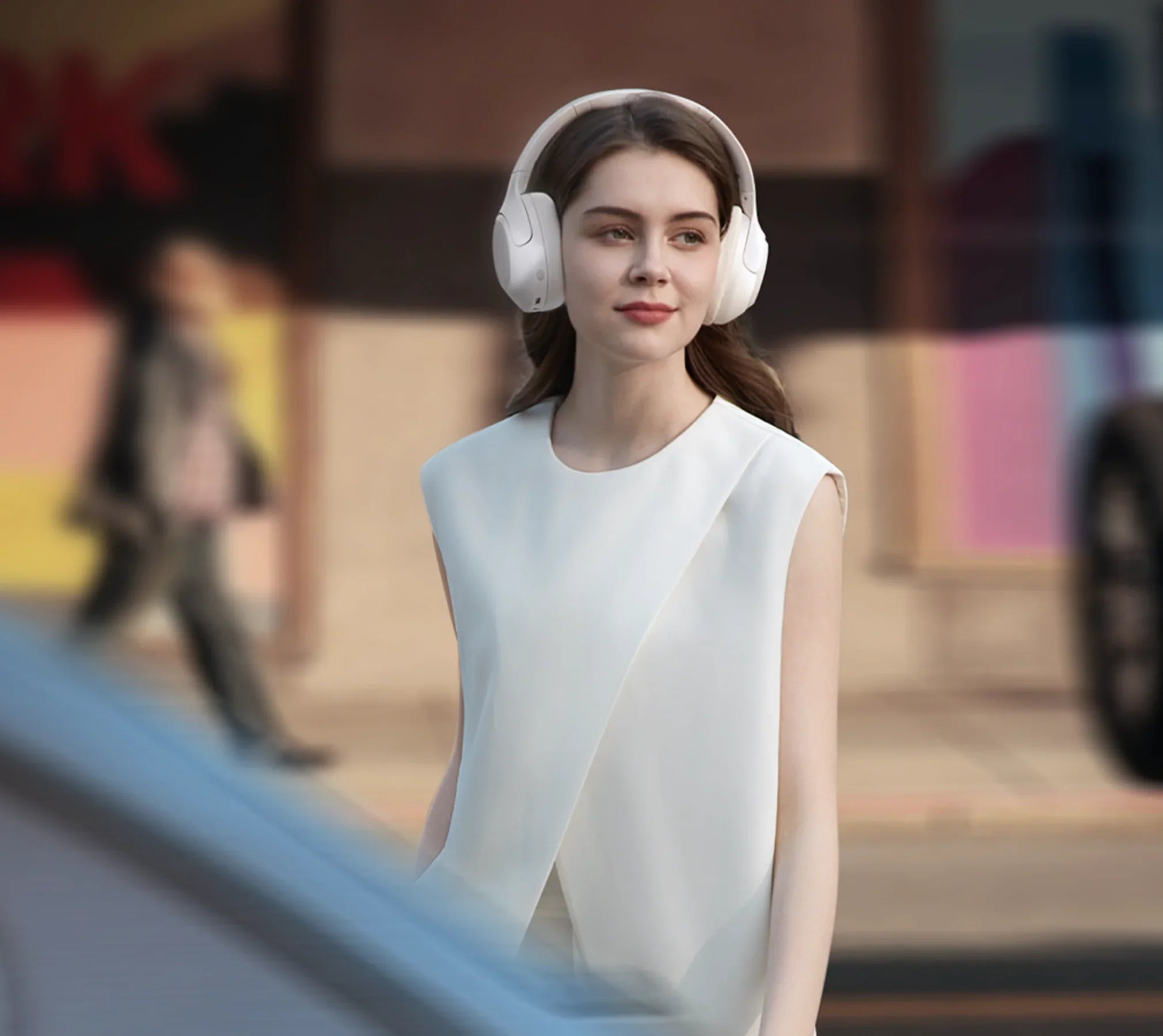 Donna con cuffie over-ear bianche in ambiente urbano, moda elegante, tecnologia moderna