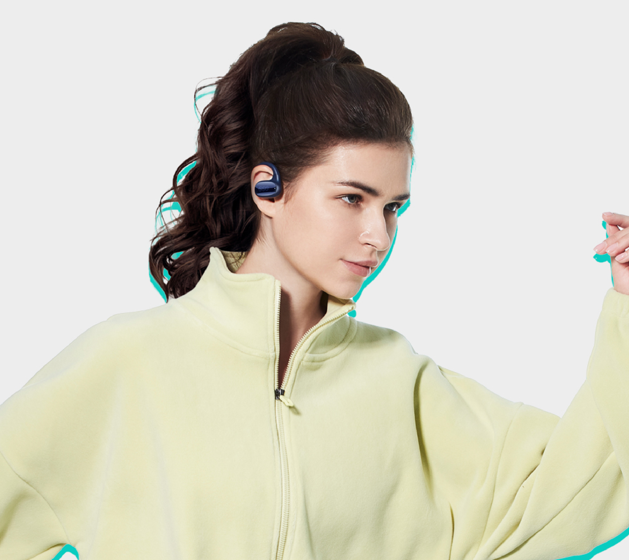Donna con capelli scuri raccolti in uno chignon che indossa cuffie sportive blu e una giacca da allenamento giallo chiaro.