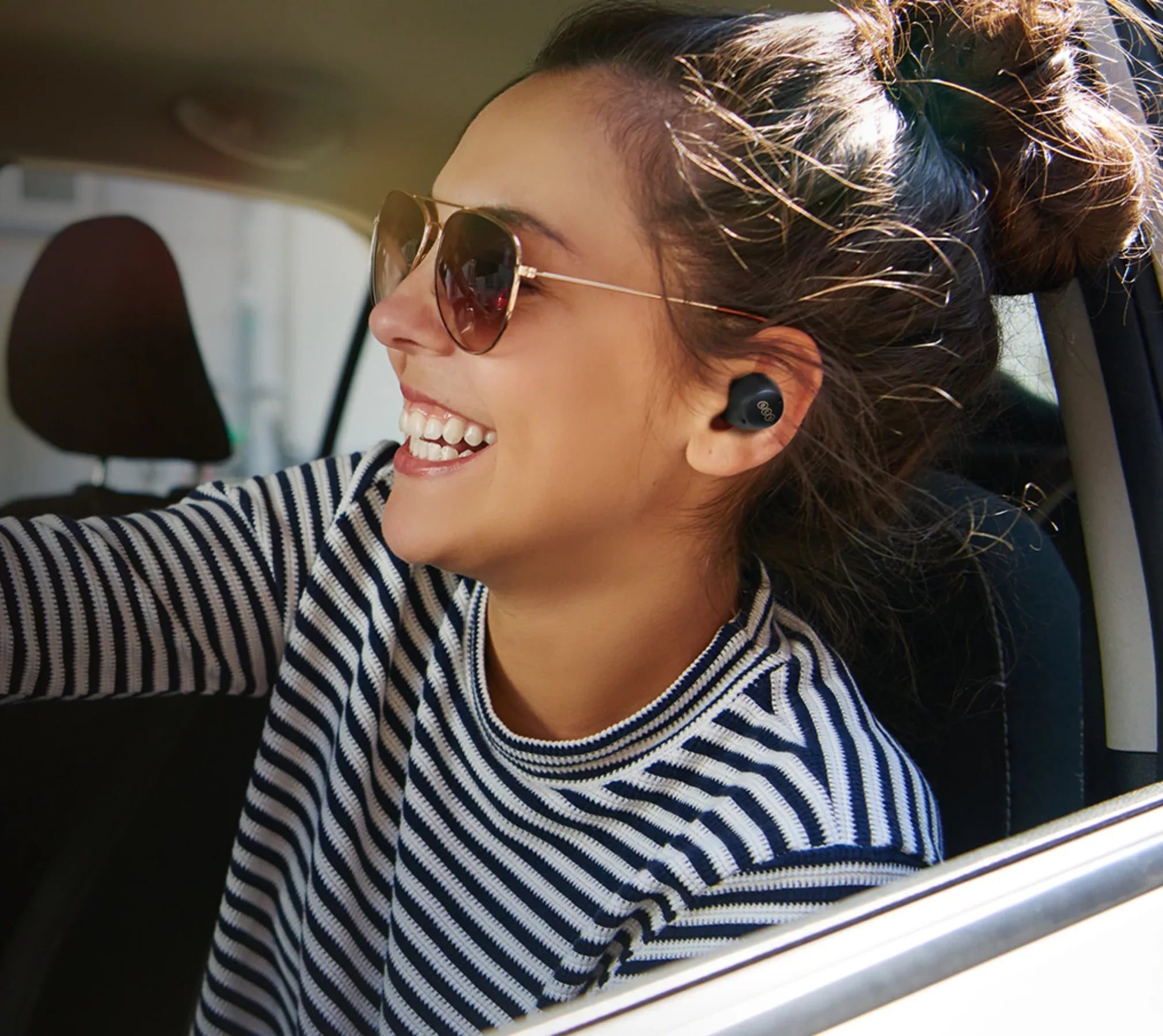 Donna con occhiali da sole e auricolari wireless in auto