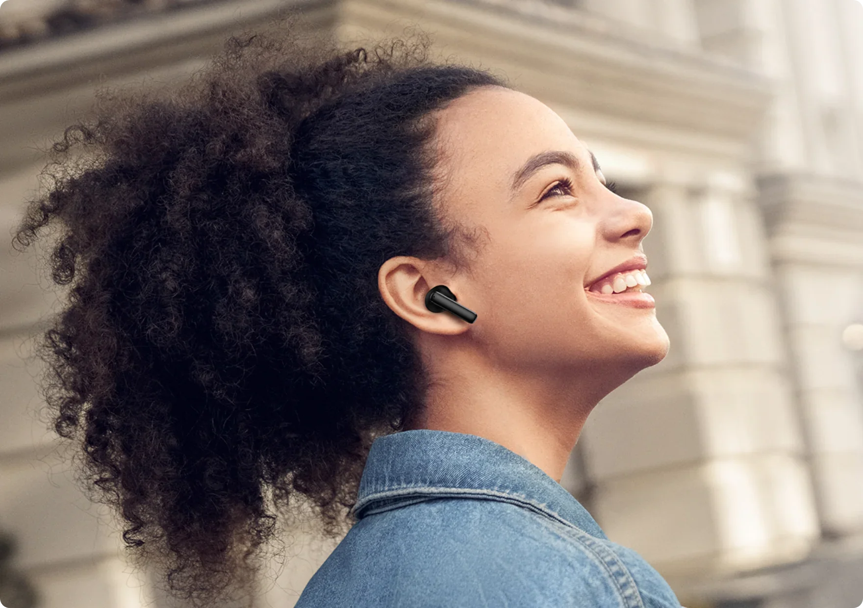 Donna sorridente con auricolari wireless neri all'aperto.