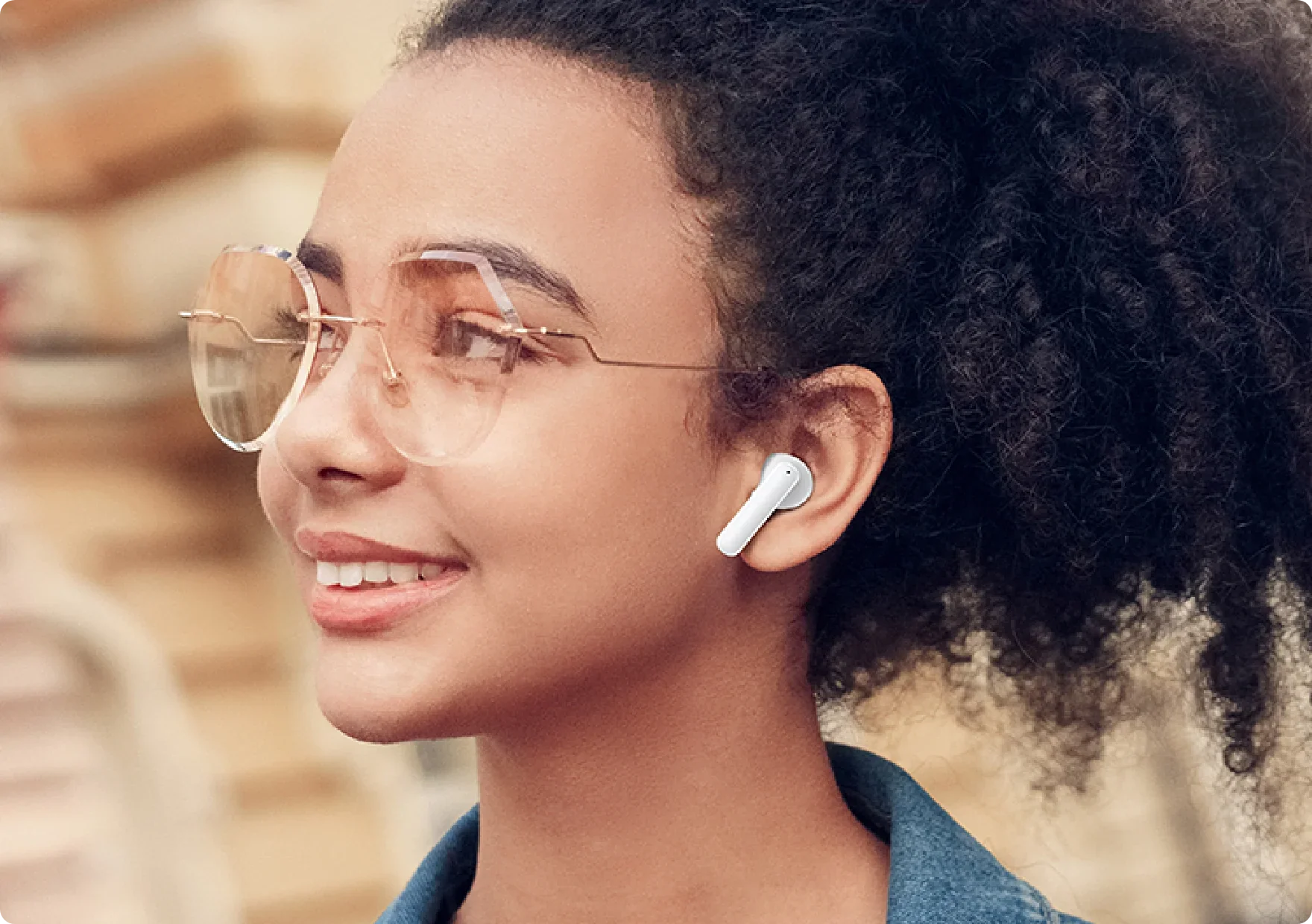 Donna con cuffie wireless bianche e occhiali da sole di profilo.