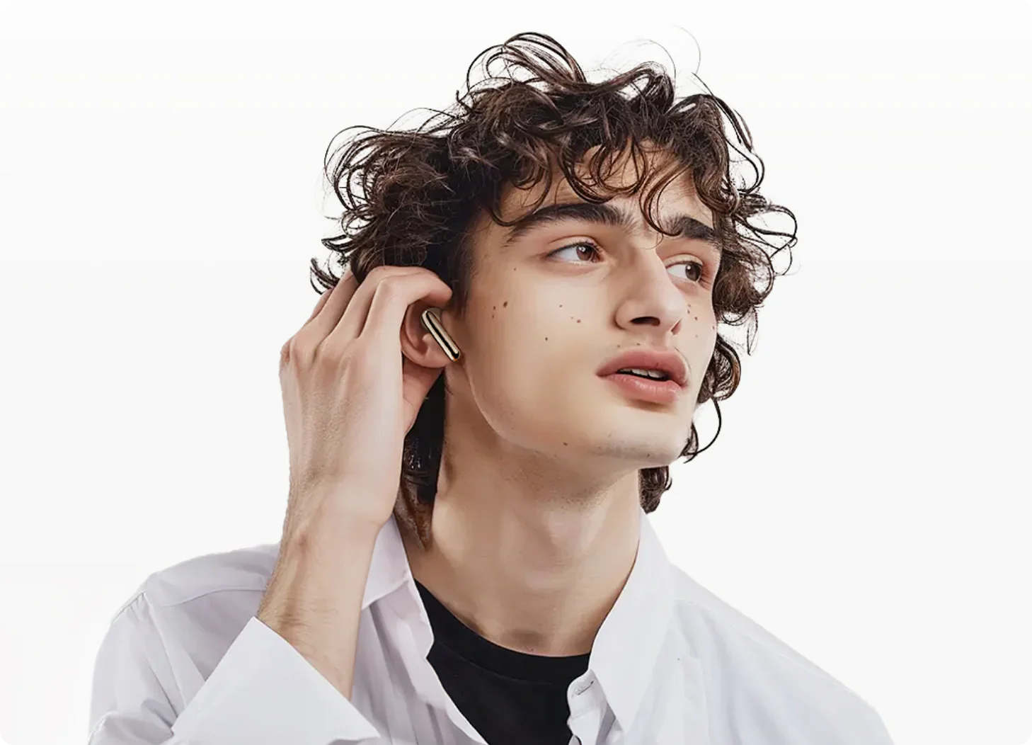 Giovane uomo con capelli ricci che indossa auricolari wireless dorati, camicia bianca, look moderno e lifestyle.