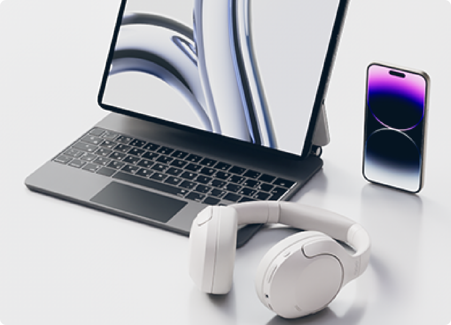 Set moderno per laptop con cuffie bianche e smartphone su tavolo chiaro.