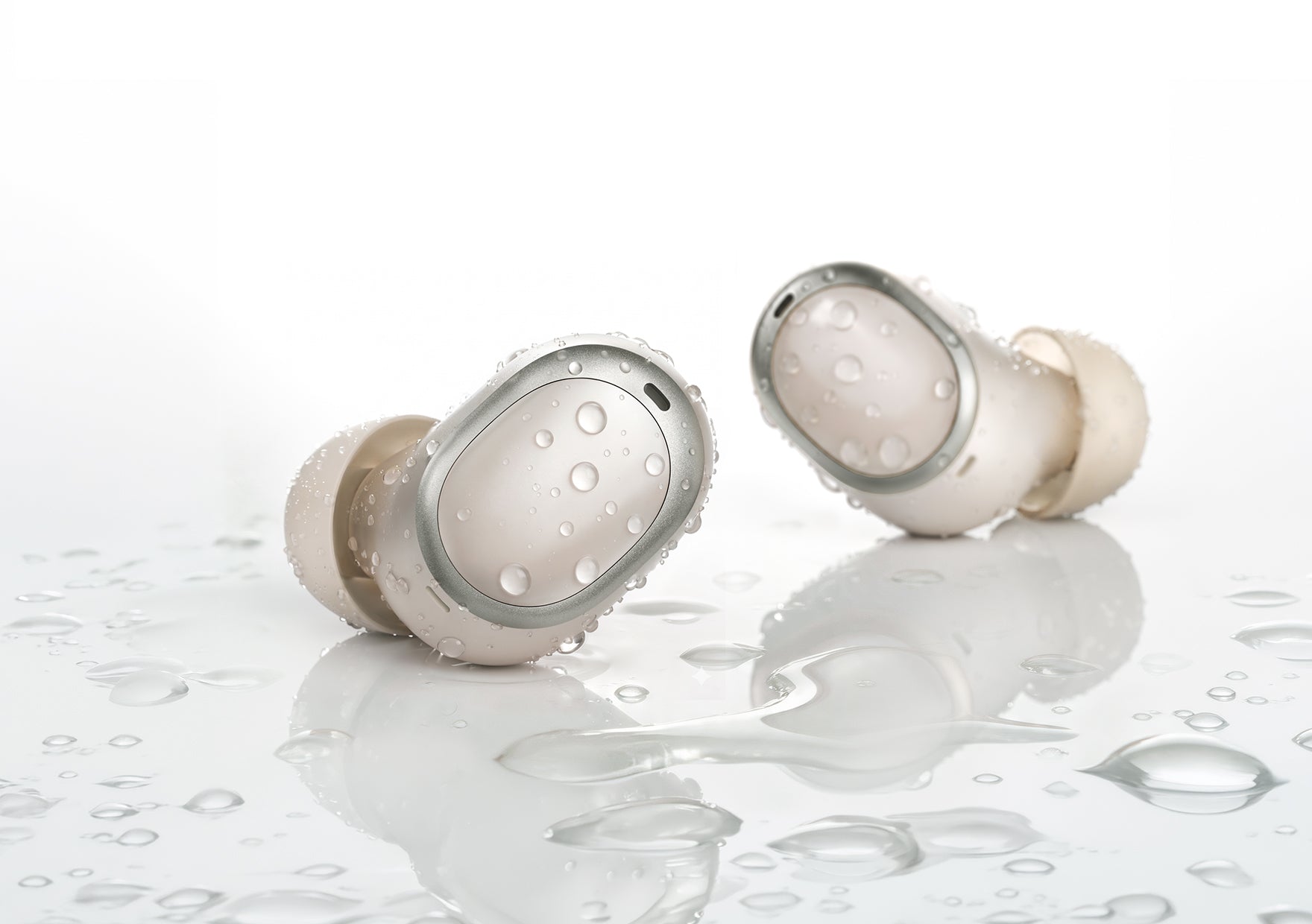 Auricolari in-ear bianchi impermeabili con gocce d'acqua su superficie riflettente.