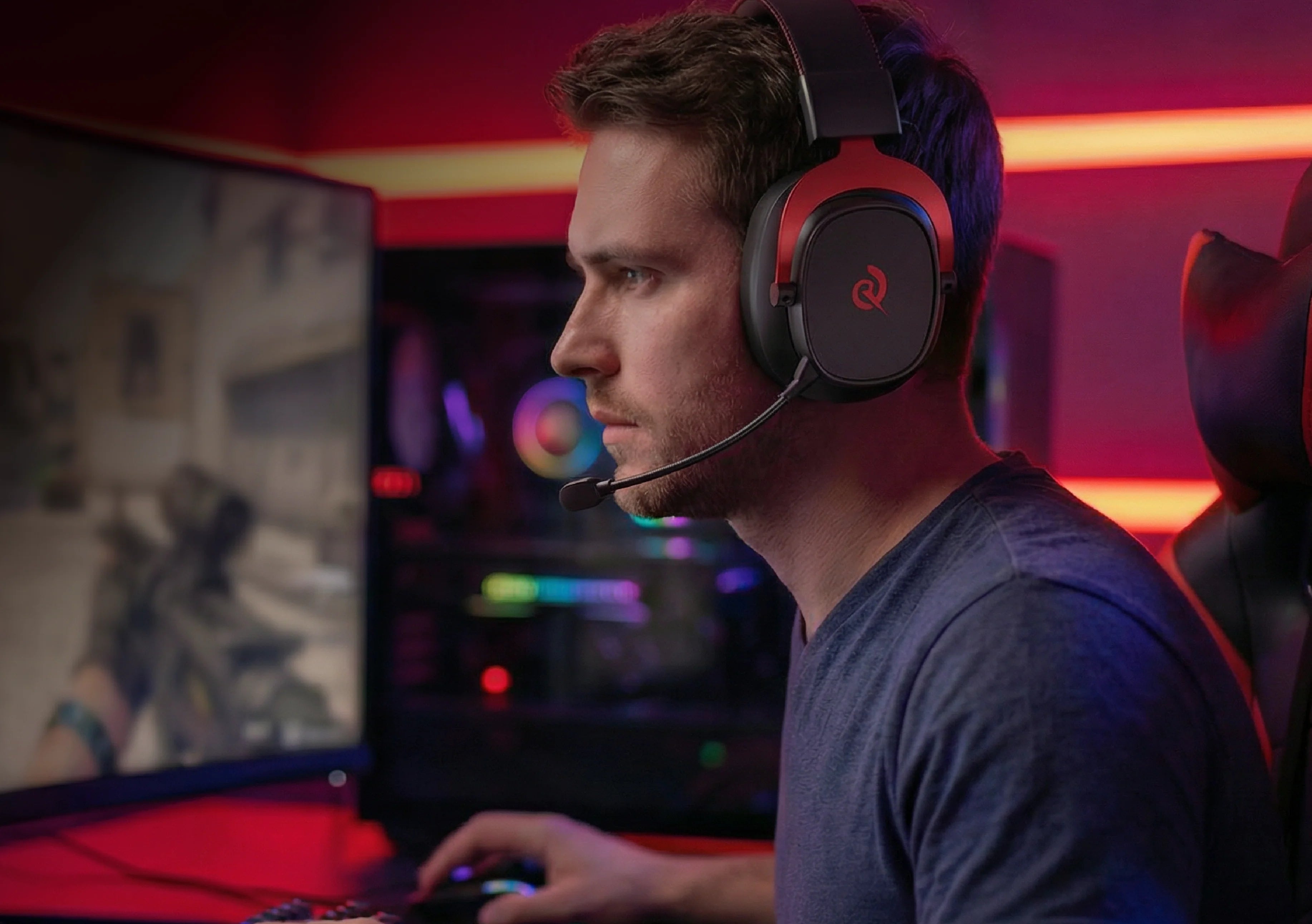 Uomo con cuffie da gaming e microfono davanti al monitor del PC, illuminazione RGB luminosa sullo sfondo